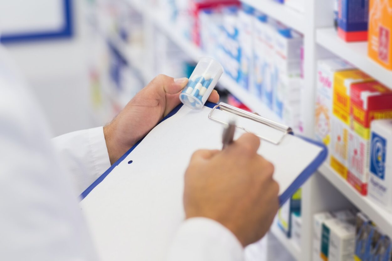 Farmacéutico escribiendo en portapapeles y sosteniendo frasco de medicina en la farmacia del hospital