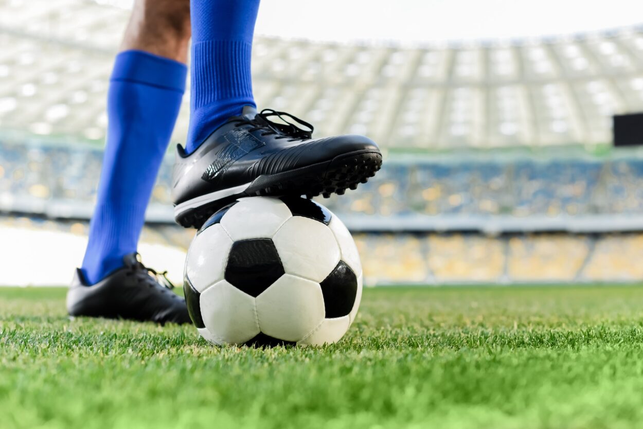 pernas de jogador de futebol profissional em meias azuis e chuteiras na bola no estádio