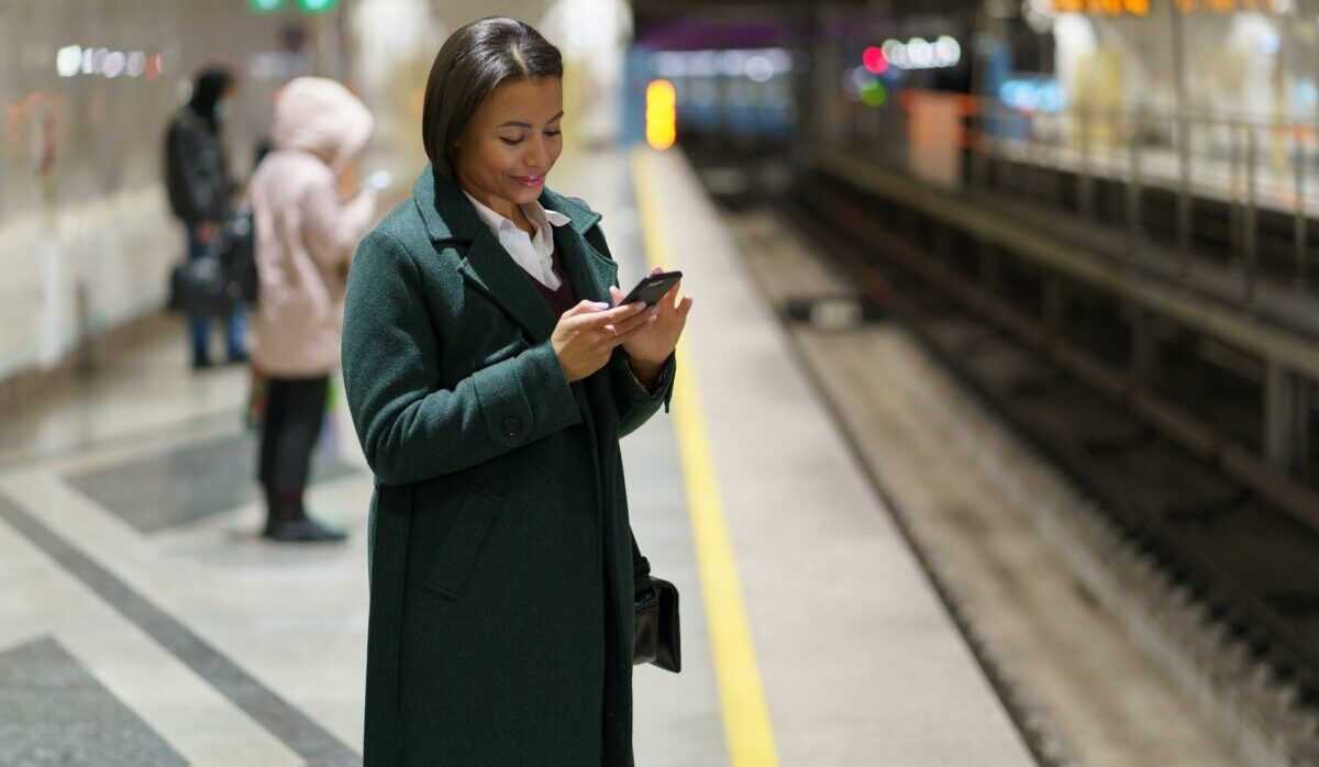 Lächelnde Afro-Frau am U-Bahnsteig mit Smartphone, schwarze Frau, die drahtloses Internet in der U-Bahn nutzt