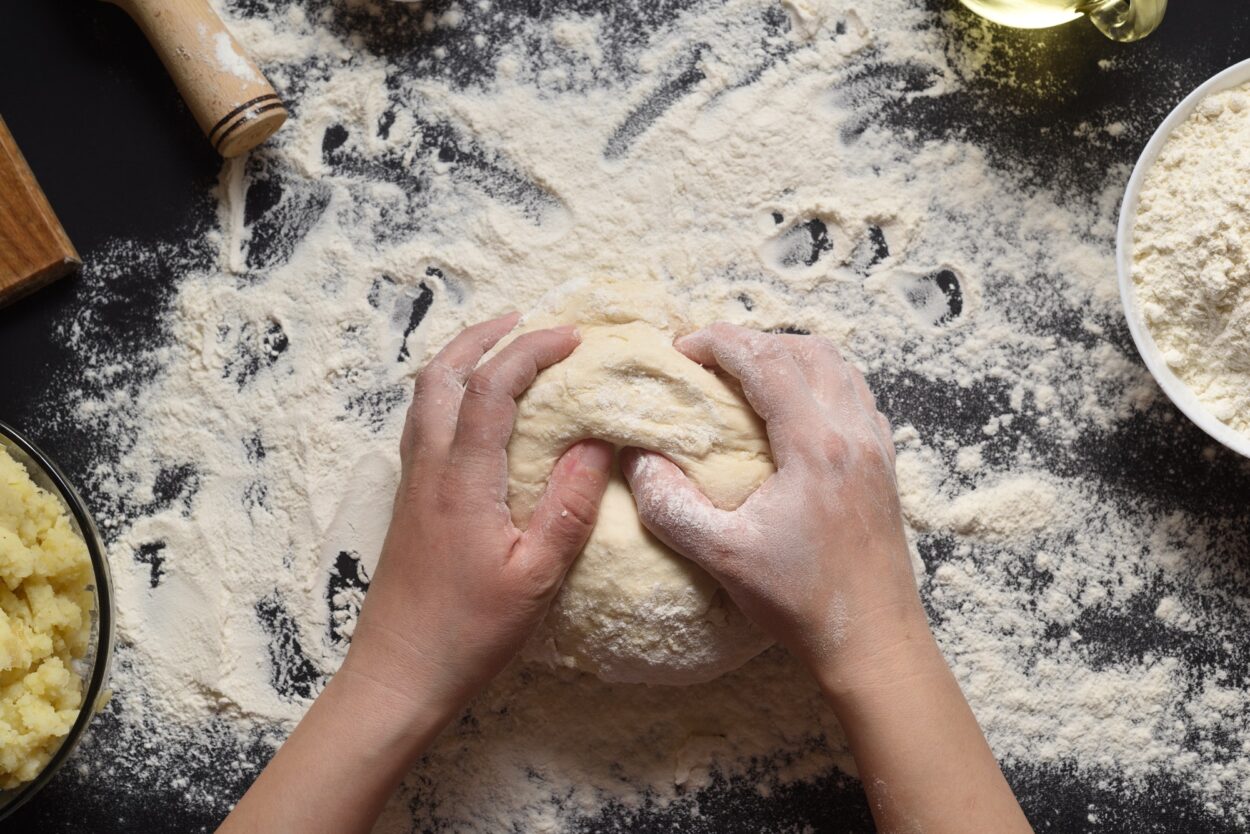 Pizzateig oder Backen auf einem dunkelschwarzen Hintergrund aus Holz. Brot, Pizza, Nudeln backen.