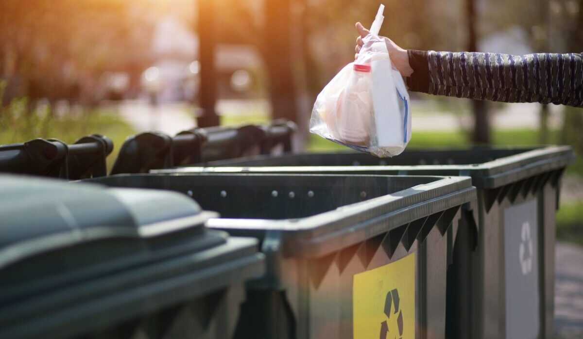 Hand mit einer Tüte Plastikmüll über Container zur Trennung und Sortierung