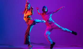Two dancers, young man and woman dancing hip-hop in casual sports youth clothes on gradient purple