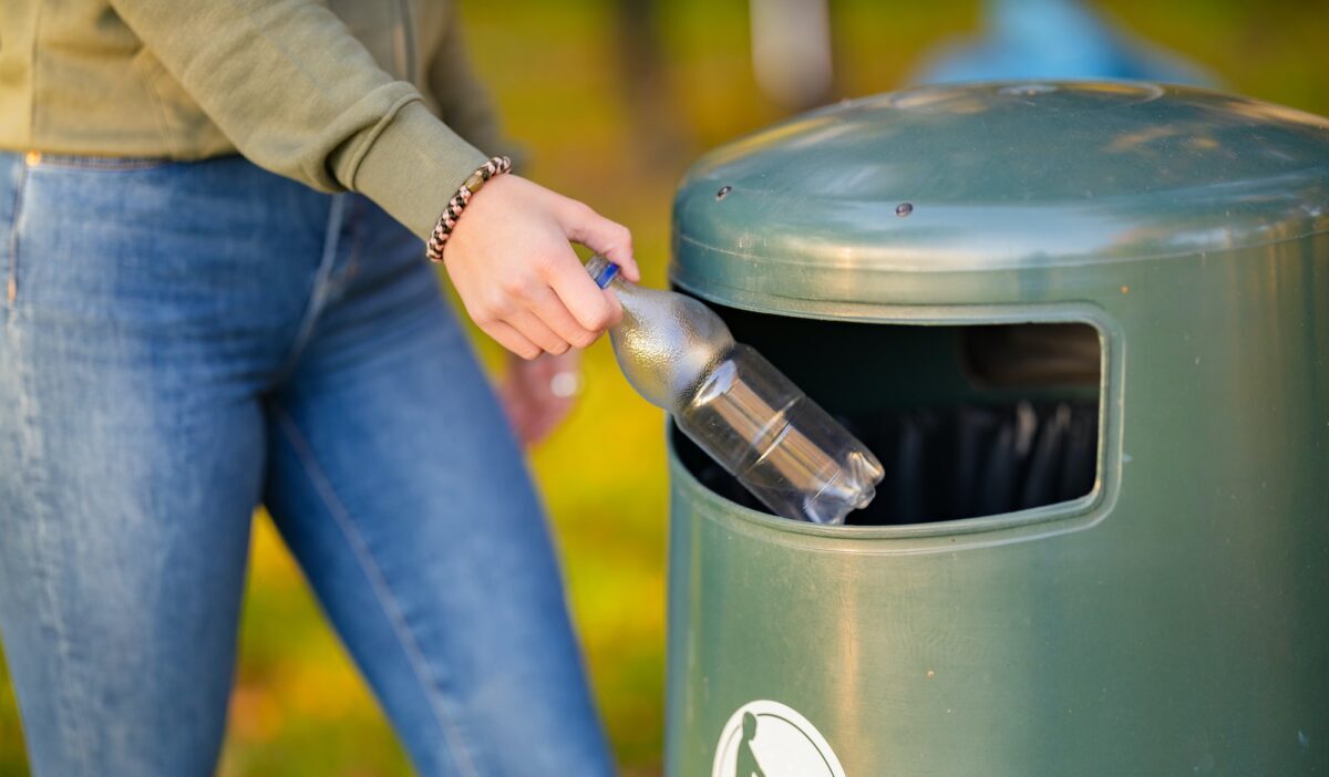 Midsection of woman putting bottle in garbage bin