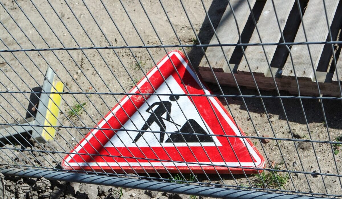 Road sign. Work in progress. Laying on the ground and behind the fence.