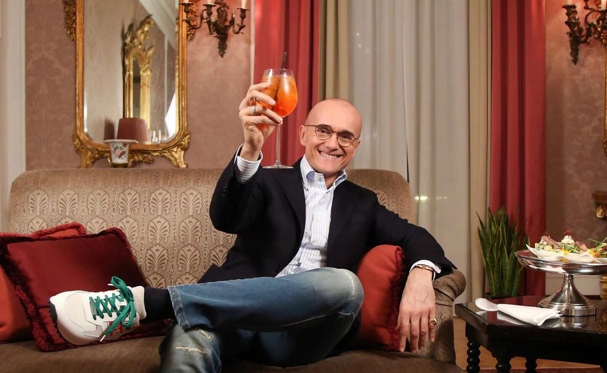 Alfonso Signorini em um sofá com uma taça de vinho na mão