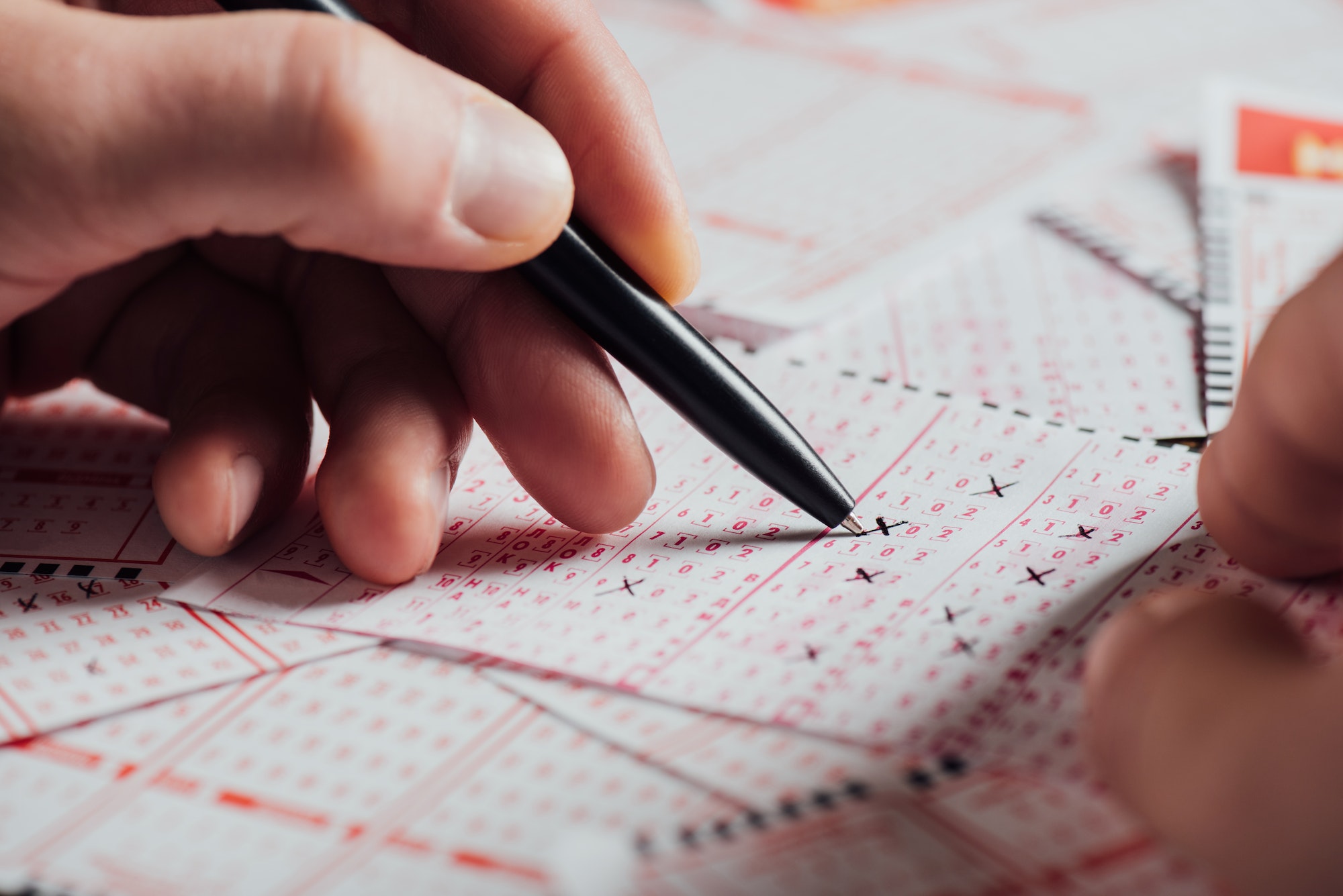 cropped view of gambler marking numbers in lottery tickets with pen