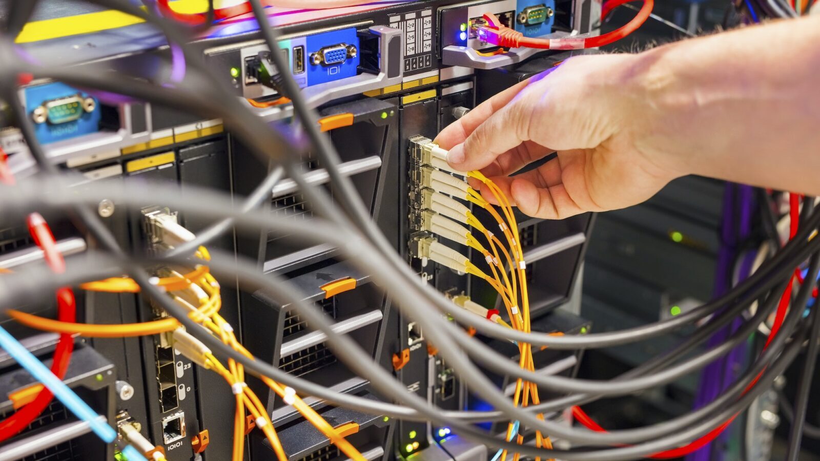 Hand, die das Glasfaserkabel in den Switch im Rechenzentrum einsteckt