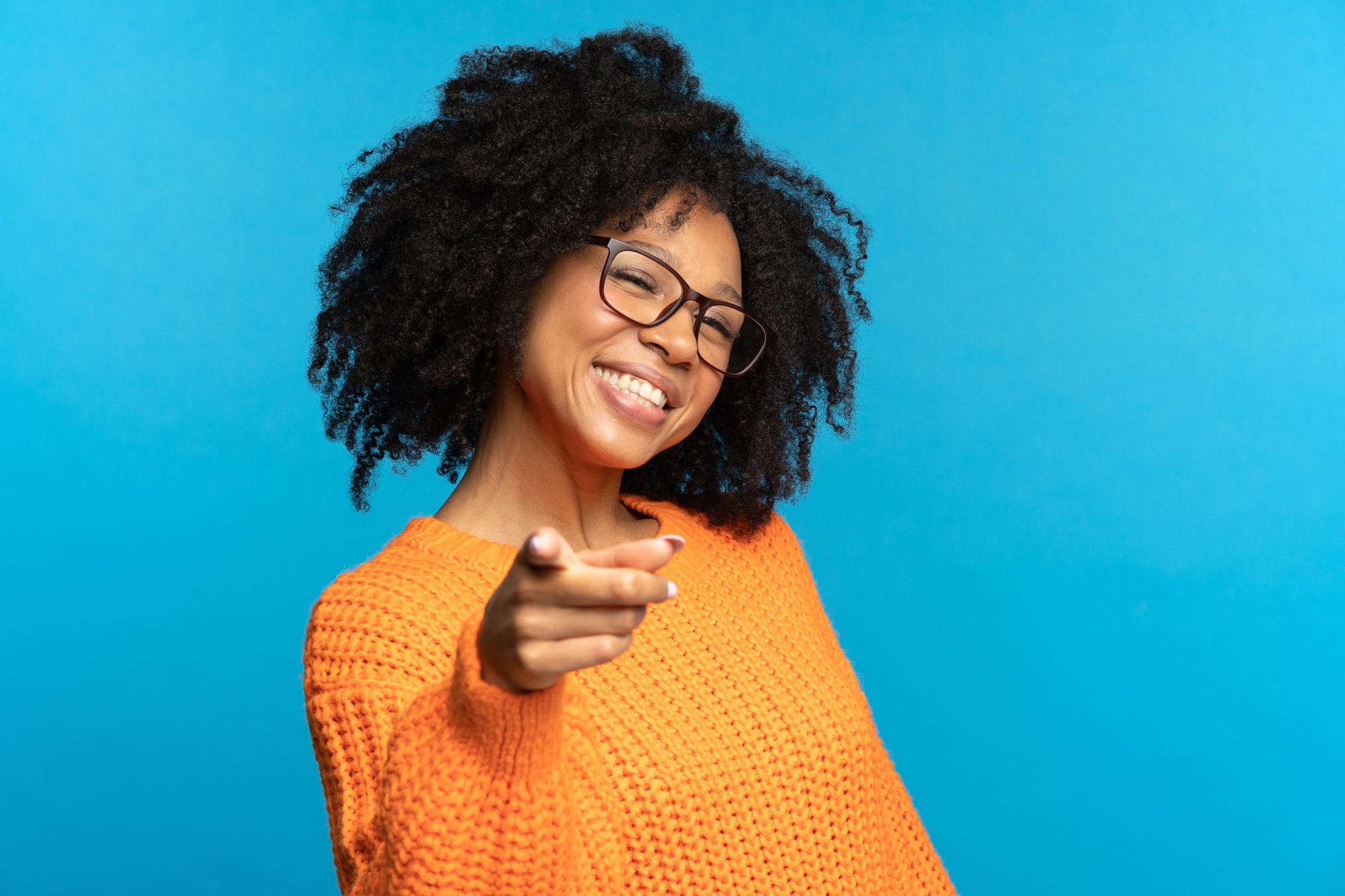 Una alegre chica afroamericana señala con el dedo eligiéndote sonriendo. Oferta de puesto de trabajo, concepto de carrera.