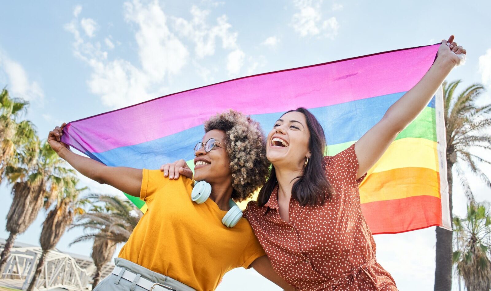 Young lesbian couple celebrates pride day with rainbow flag. Concept of homosexuality, gay.