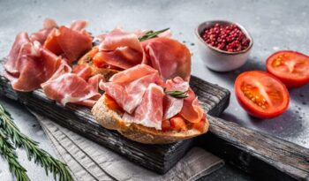 Spanische Tapas - Toast mit Tomaten und gepökelten Scheiben Iberico-Schinken auf Holzbrett.