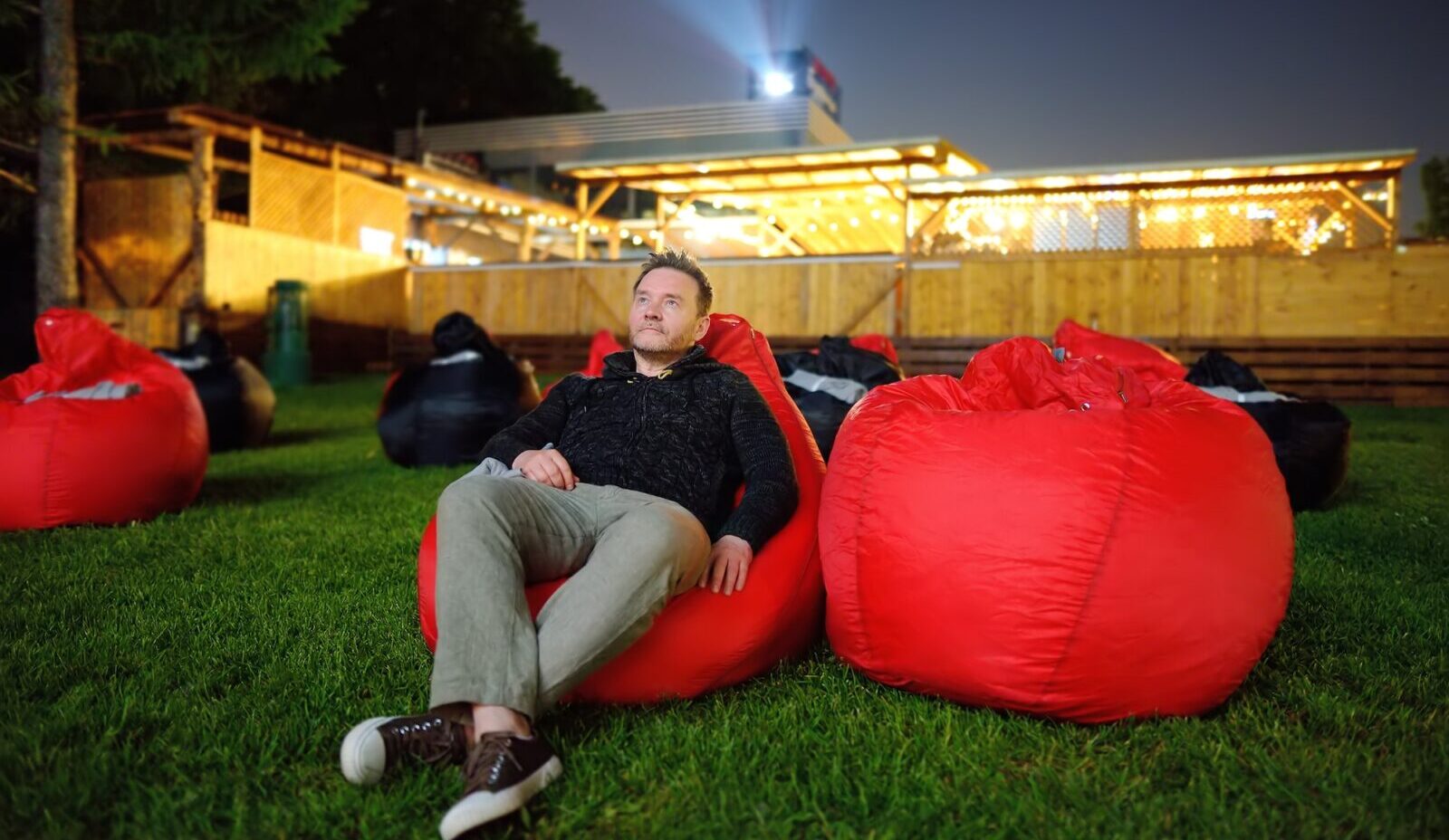 Handsome man laying on pillow on grass and watching movie at outdoor cinema in public park.