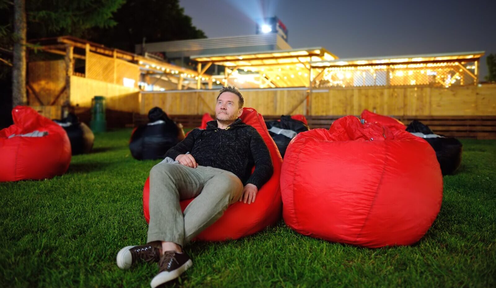 Hübscher Mann, der auf einem Kissen im Gras liegt und sich im Freiluftkino im öffentlichen Park einen Film ansieht.