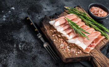 Prosciutto crudo parma ham, dry cured pork meat on a wooden board. Black background.