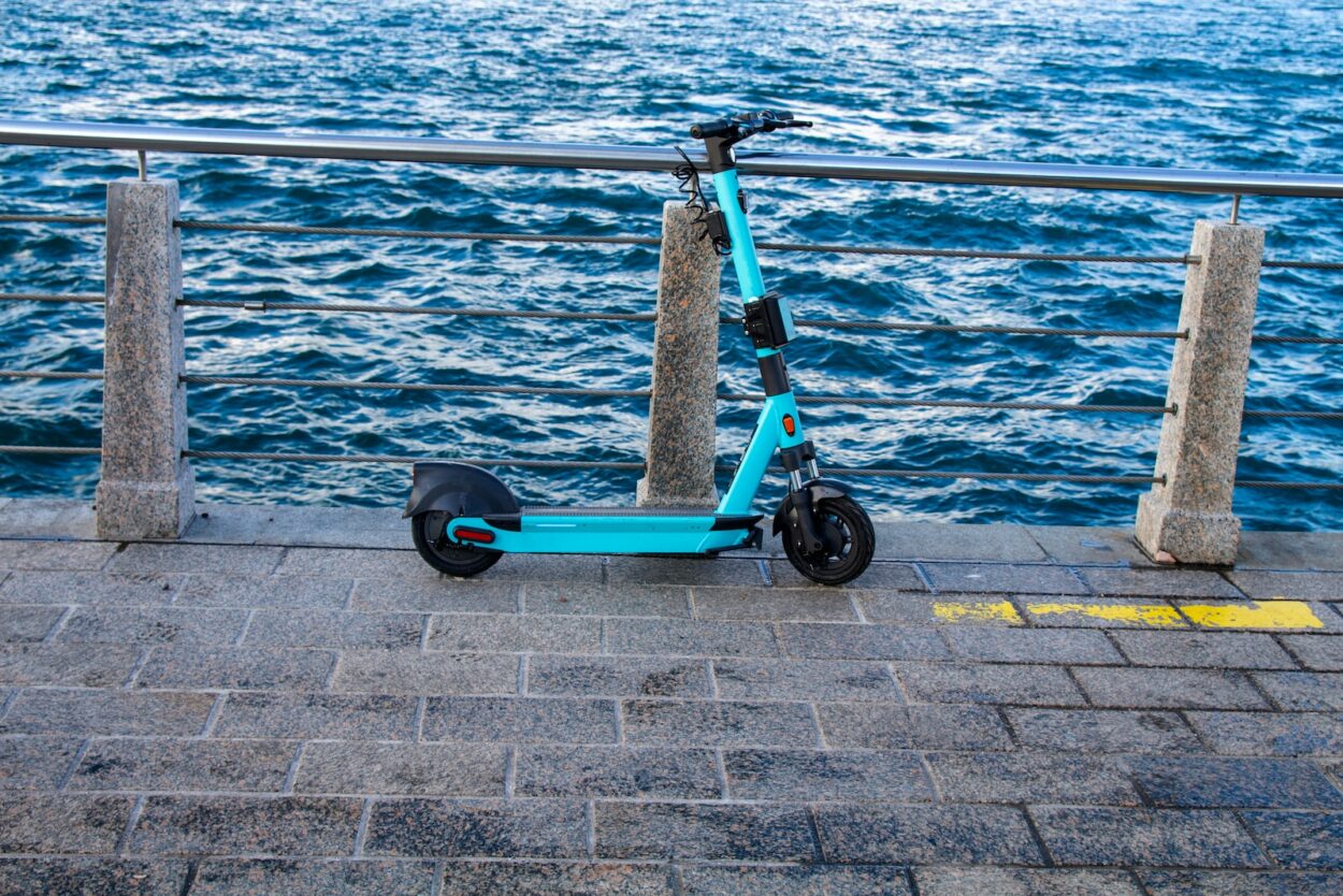 a blue scooter parked on a sidewalk next to a body of water