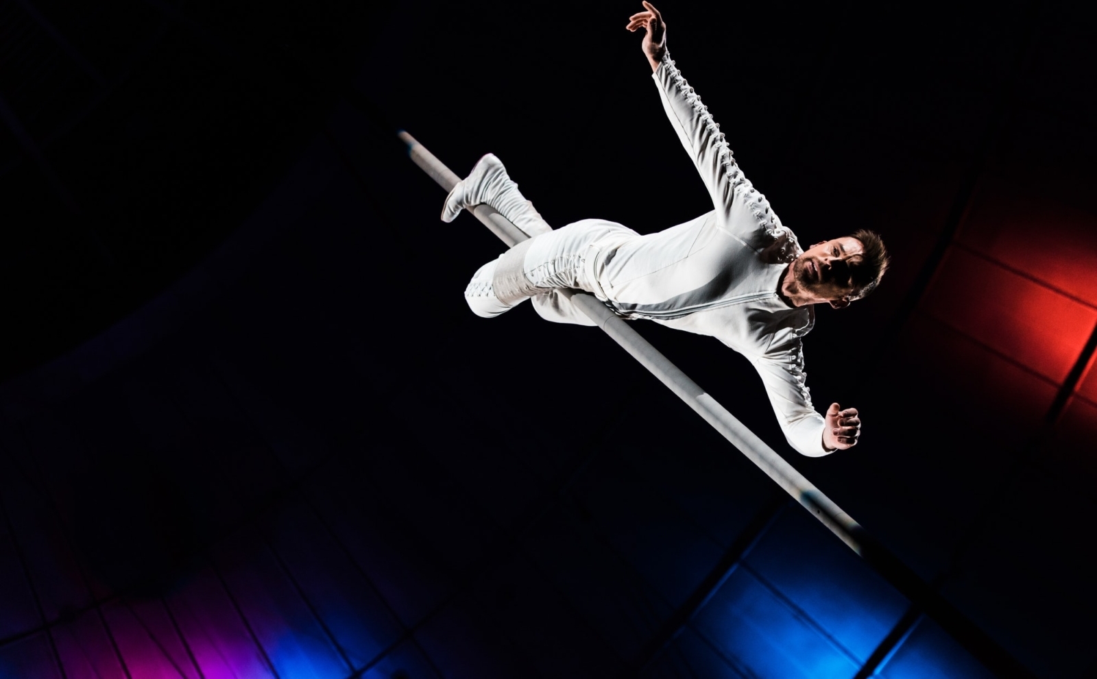 low angle view of handsome acrobat holding metallic pole with legs while performing in circus