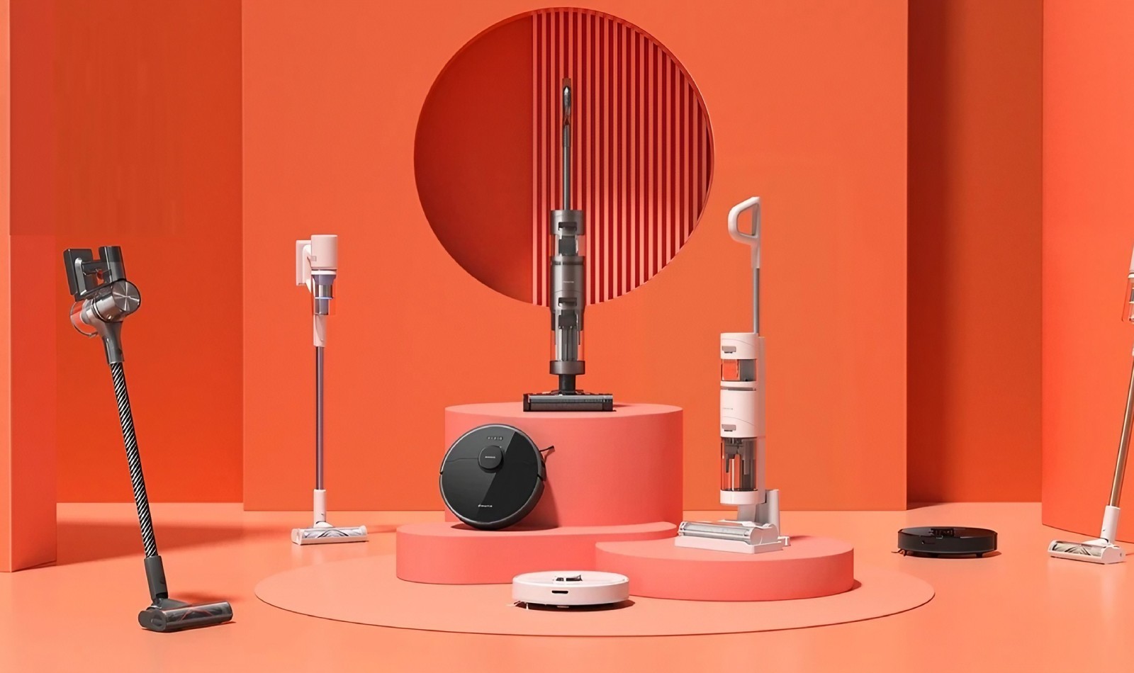 una panoramica di vari aspirapolvere a batteria e robot aspirapolvere su vari piedistalli in uno stage dal fondale arancione